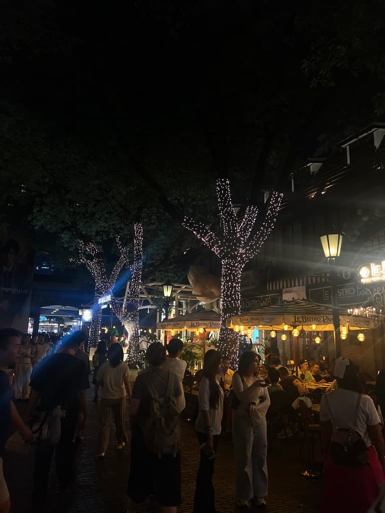 A lively restaurant street at night with illuminated trees